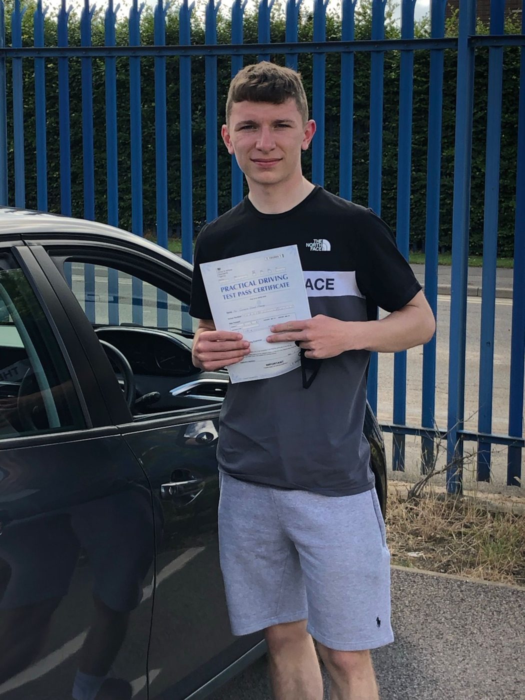 Young driver showing his driving test pass certificate beside the tuition car