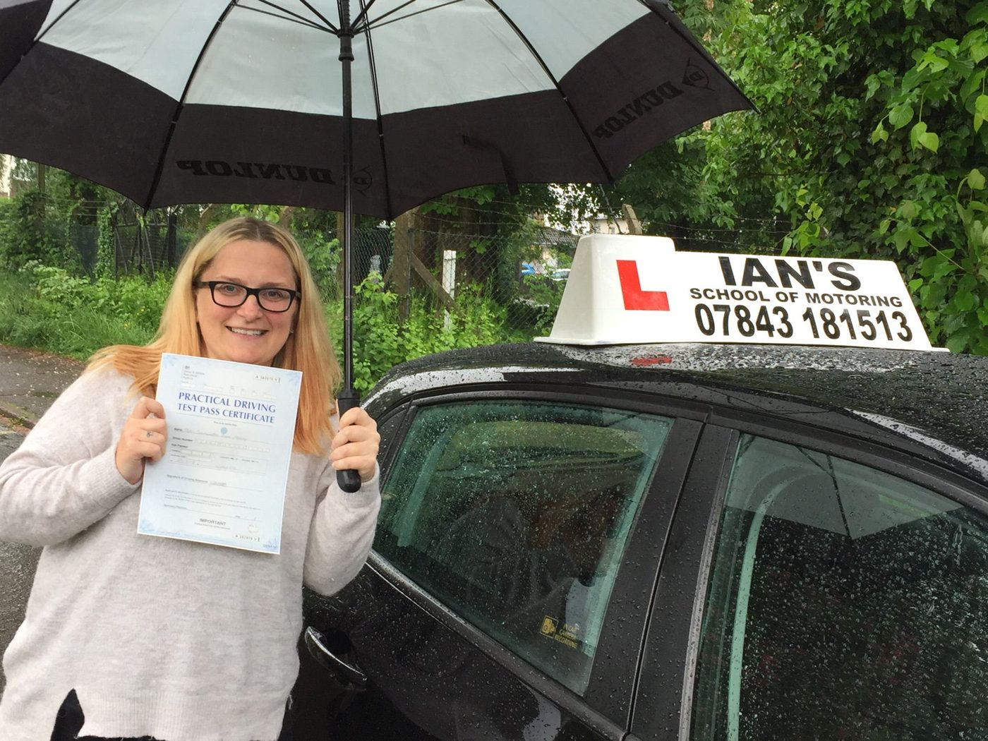 Learner holding her pass certificate under an umbrella beside Ian's tuition car