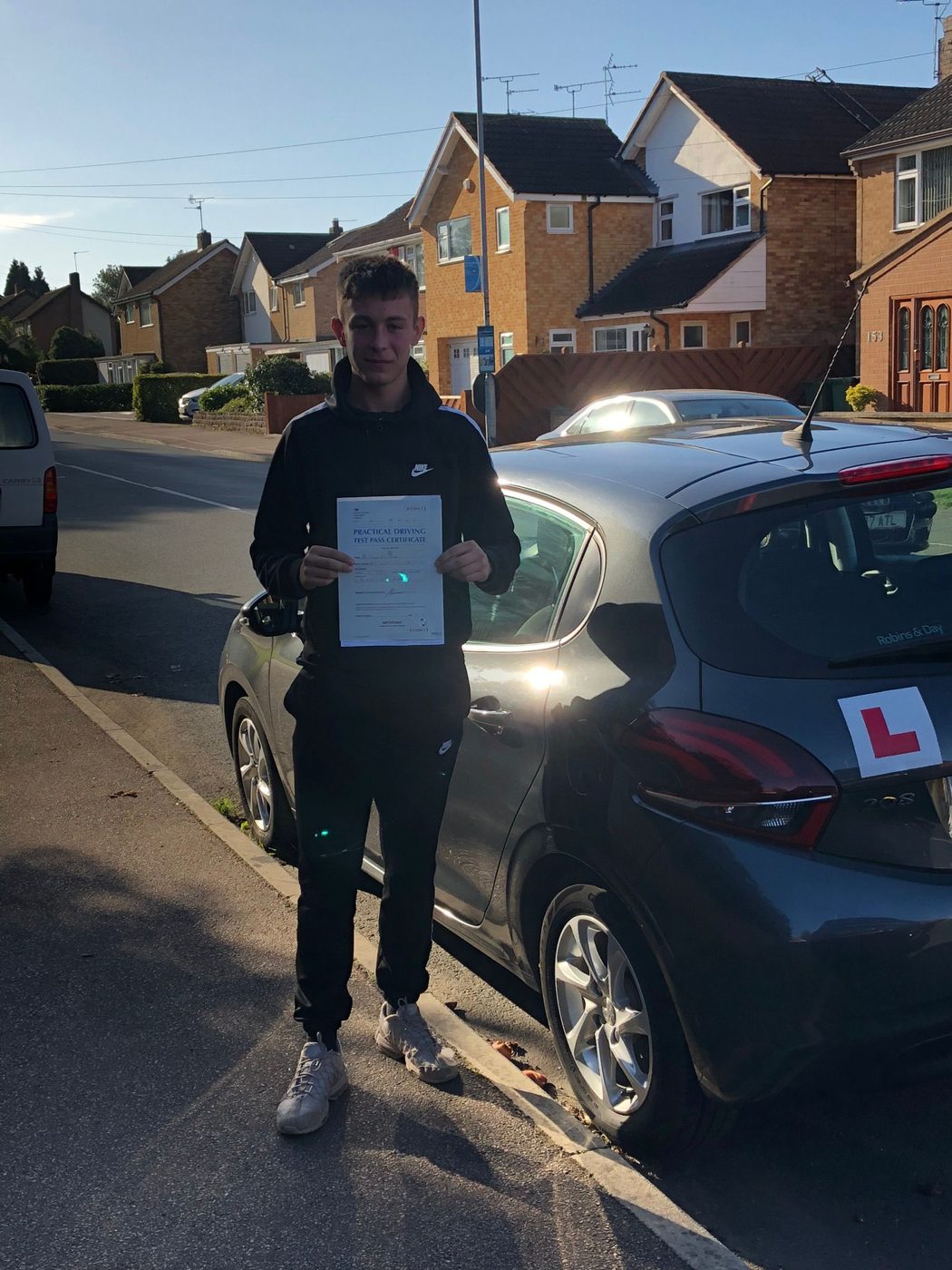 Learner holding a pass certificate on a Leicester street beside the tuition car