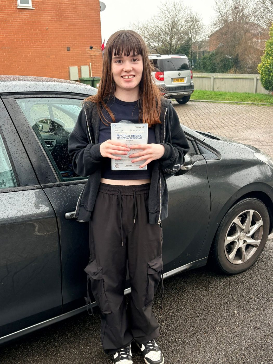 Zoe holding her driving test pass certificate beside Ian's tuition car