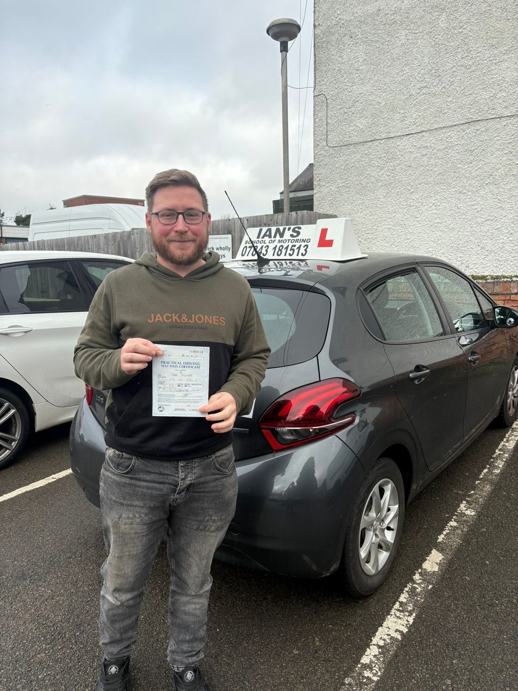Learner holding a driving test pass certificate beside the tuition car
